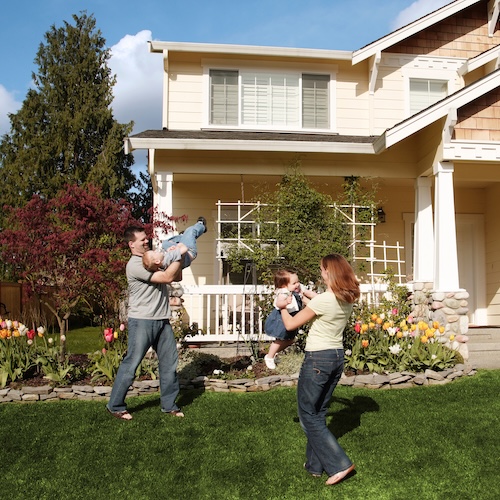 Happy family with two toddlers playing on the landscaped front lawn of new home.