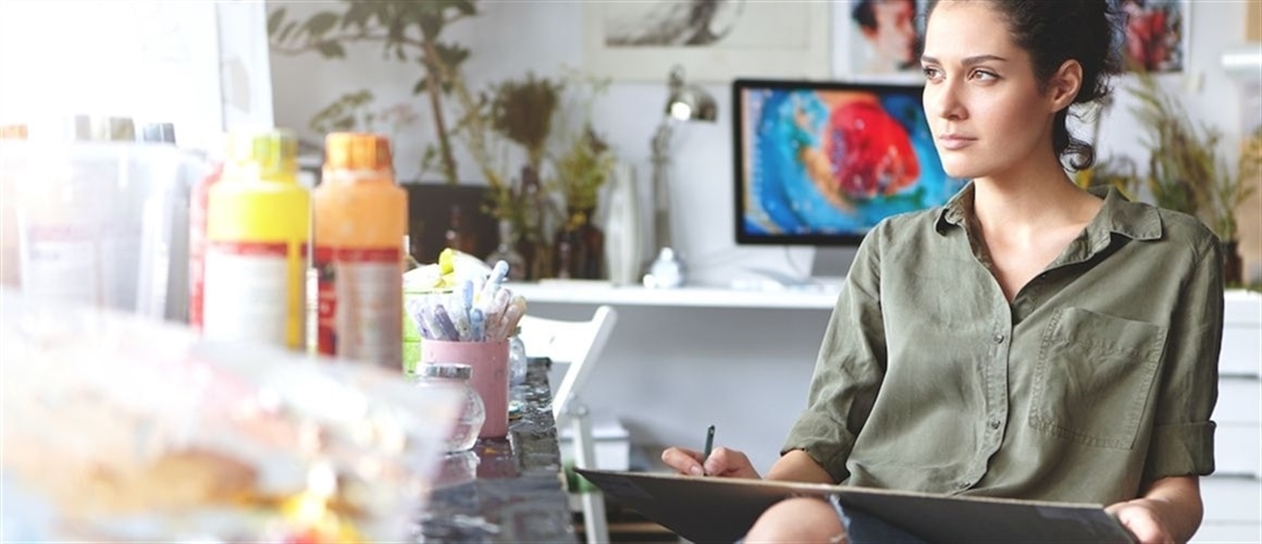 Image of woman artist at workspace, considering personal loans and staring out the window.