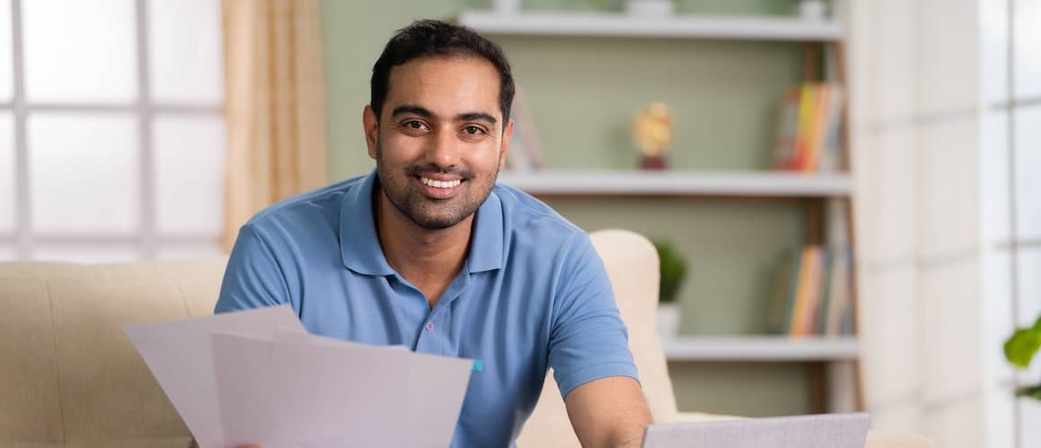 Man looks up at camera while using computer with smile on his face.