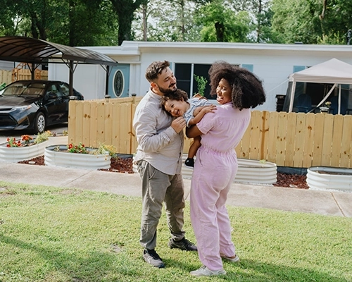 Couple holding small child, laughing in front of home.