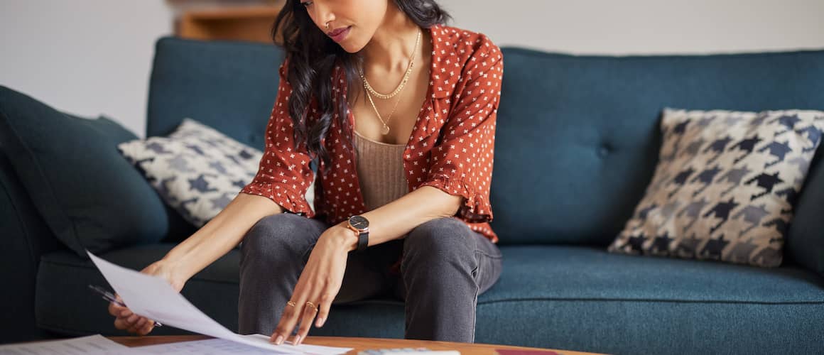 Young woman sitting on couch looking over bills on coffee table.