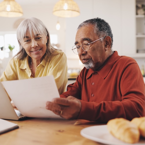 Elderly couple looking at paperwork in the kitchen and smiling.