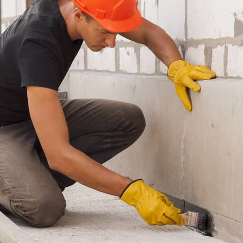 A man working on a home foundation, possibly related to construction or repair work.