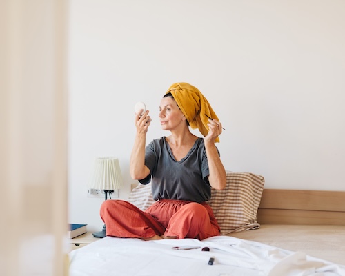 Woman in bed with towel on head looking in mirror.