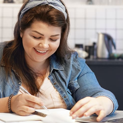 A woman working on a computer with papers scattered around.