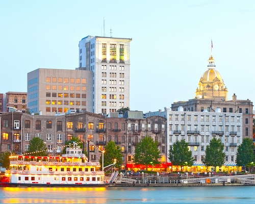 Savannah Georgia USA, skyline of historic downtown at sunset with illuminated buildings and steam boats.