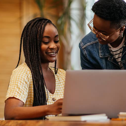 A teacher helping her student in researching student loans on laptop.