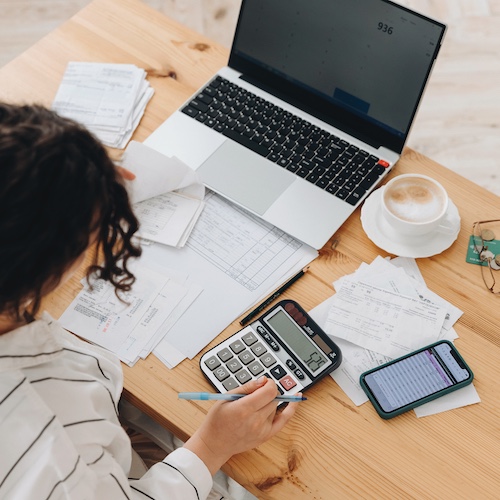 Woman budgeting at a desk with a calculator, bills, coffee, and a laptop.