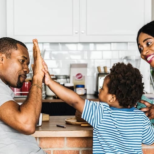 Dad giving high five to son while mother is smiling in kitchen.