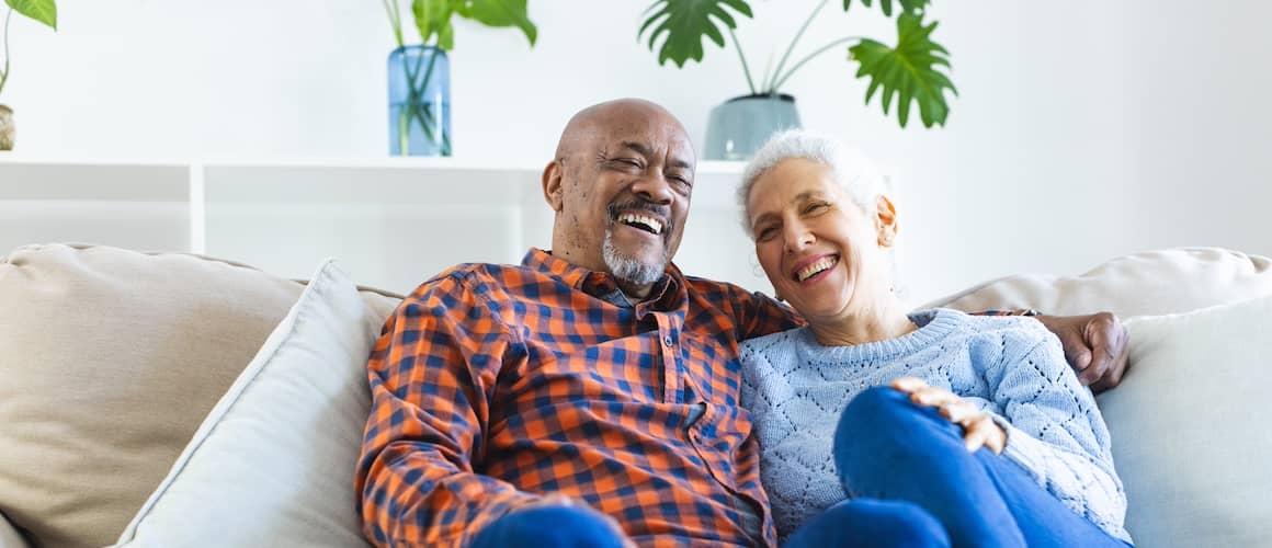 Older couple snuggling on plush couch and smiling.