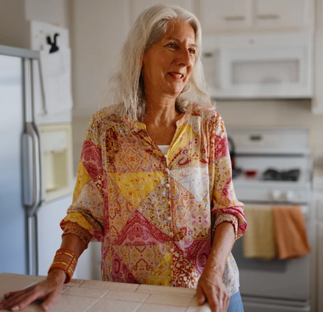 Older woman standing in a kitchen, smiling with hands resting on a countertop