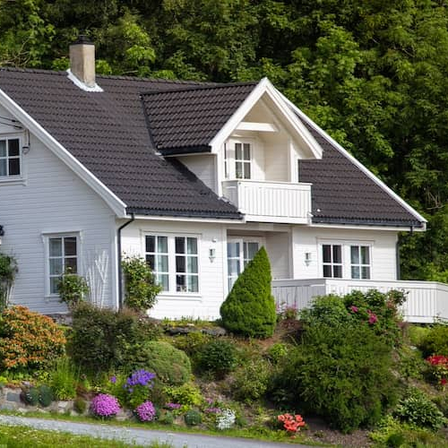 Large white house with colorful landscaping on a hill.