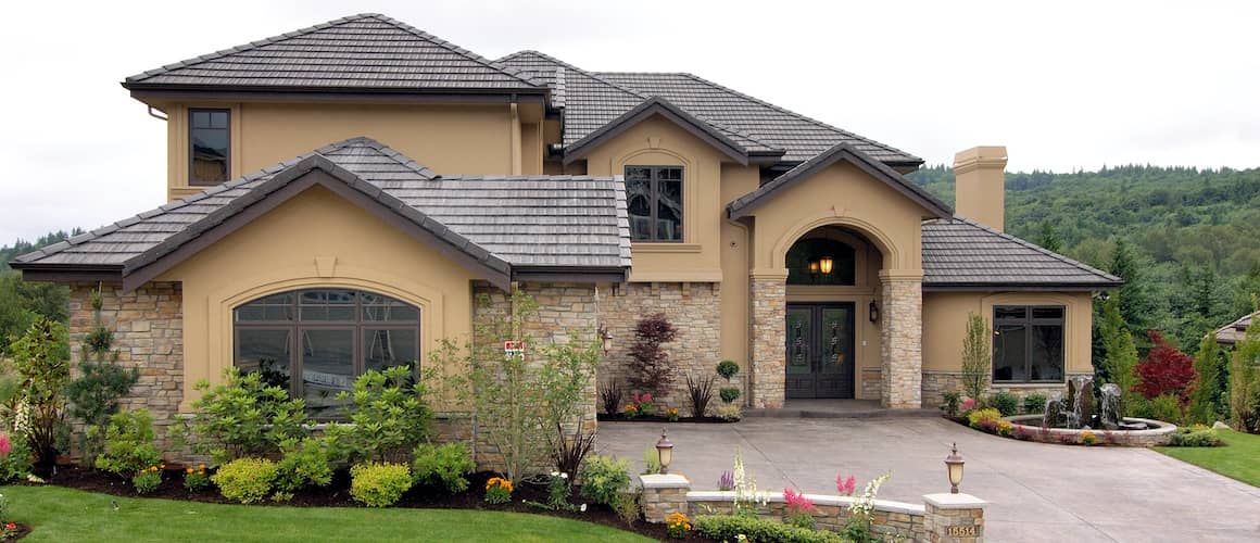 A light tan home with a black roof and stone driveway, showcasing exterior home details.