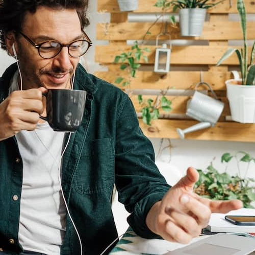 Man working a laptop, drinking coffee at a cafe with a living wall behind him.