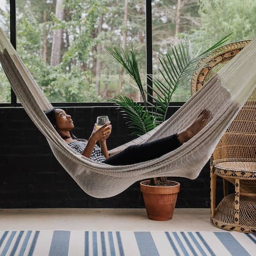 Woman laying in hammock hanging in enclosed sun porch surrounded by trees.