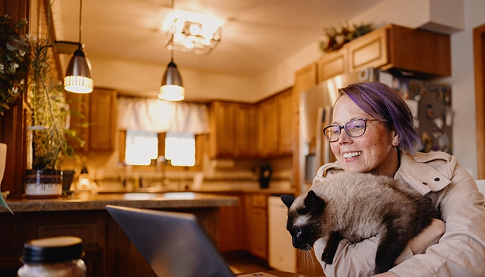 Person sitting at computer smiling and holding cat.