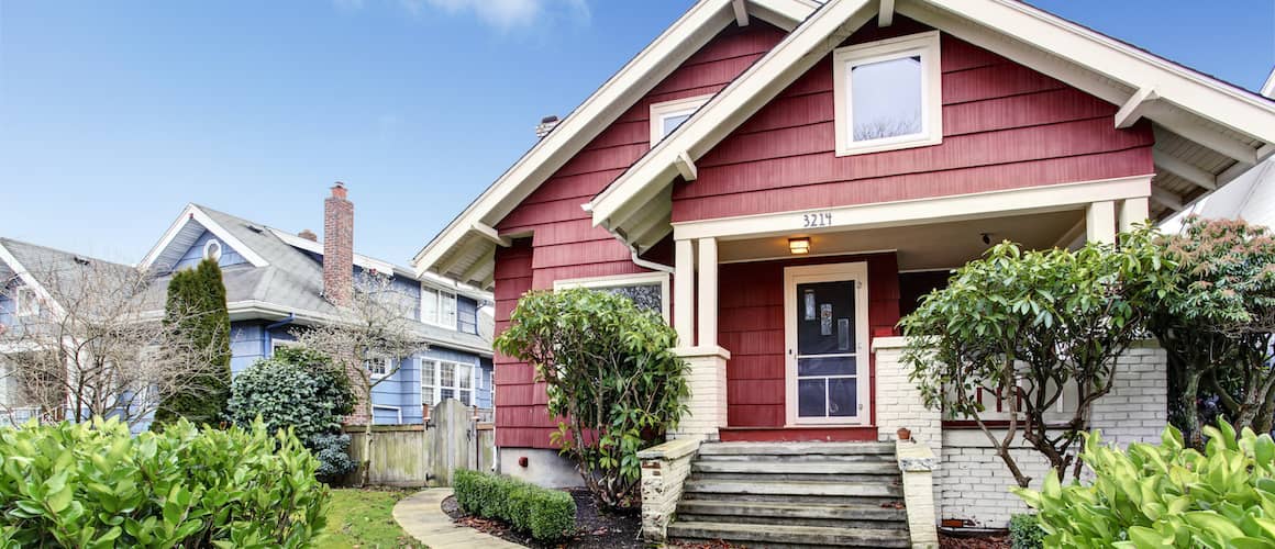 A charming red house with a welcoming front porch and a well-maintained front yard.