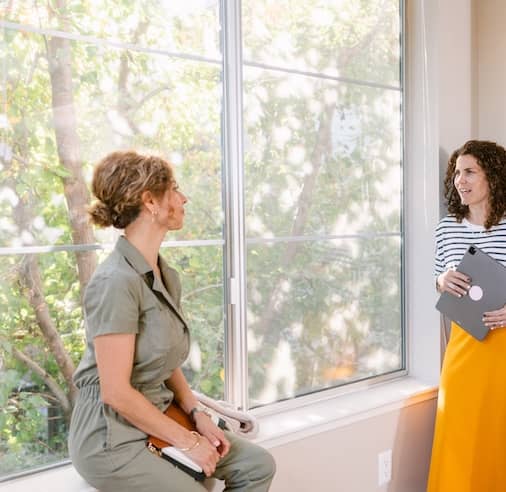 Raltor and client chatting by a large window of a home being shown for sale.