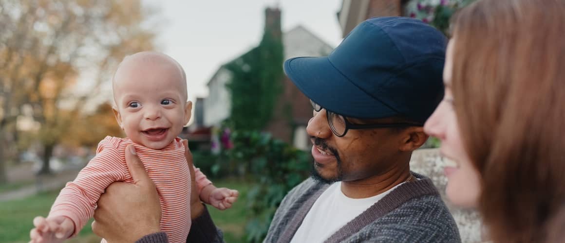 A mother and father holding their smiling baby outside of their home.