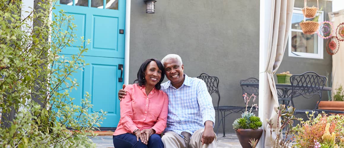 A middle aged Afro-American Couple sitting and smiling in the backyard of their house.