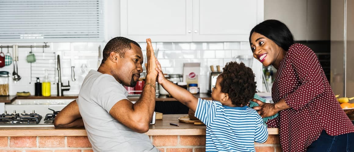 Happy family standing in kitchen, parents may help kids buy home.