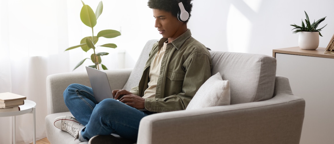 Image of man wearing headphones, staring down at laptop on couch.