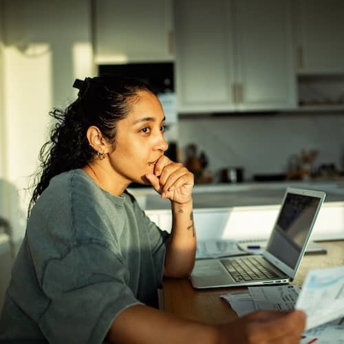 Woman paying bills at kitchen table and working on laptop.
