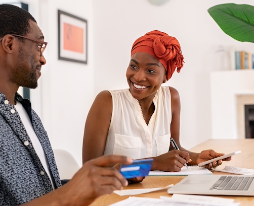 Couple smiling at one another while looking at documents on open laptop.