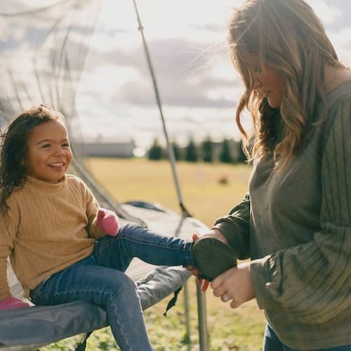 A mother adjusts her child’s shoe while she sits on a trampoline.