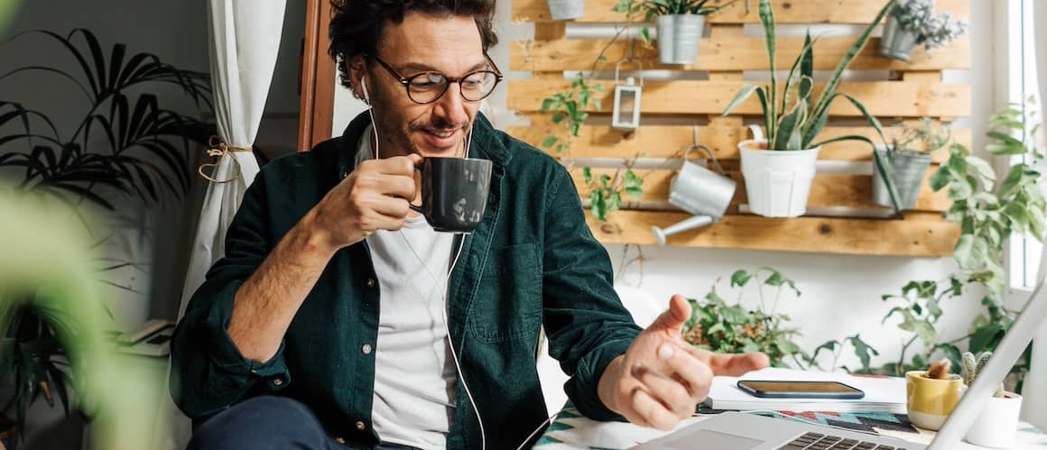 Man working a laptop, drinking coffee at a cafe with a living wall behind him.