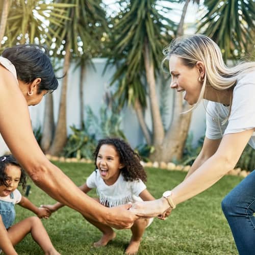 Grandma, mother and daughters laughing in a cirlce holding hands.