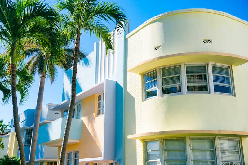 Brightly colored art deco home surrounded by palm trees.