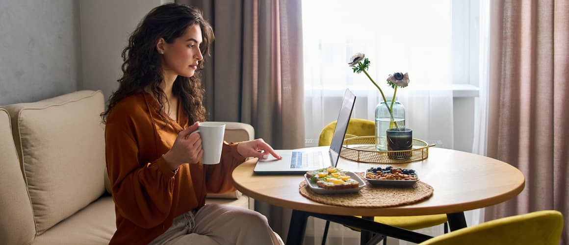 Woman sitting at breakfast table working on laptop.