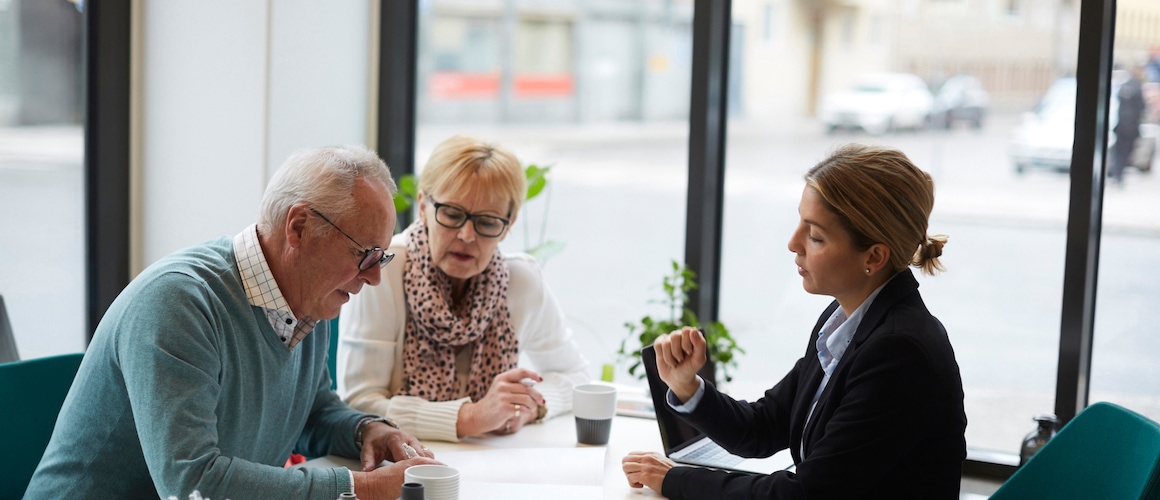 A senior couple signing paperwork with a real estate agent, depicting seniors engaging in real estate transactions.