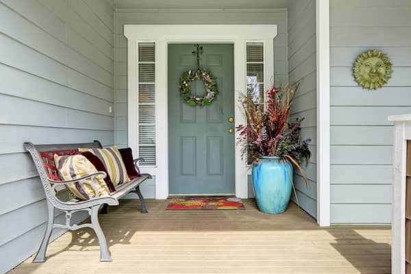 Decorated front porch of house with a bench and a large potted plant.