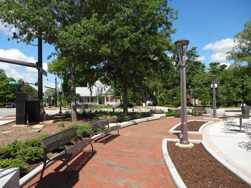 Brick pathway in a park with benches to the left side.