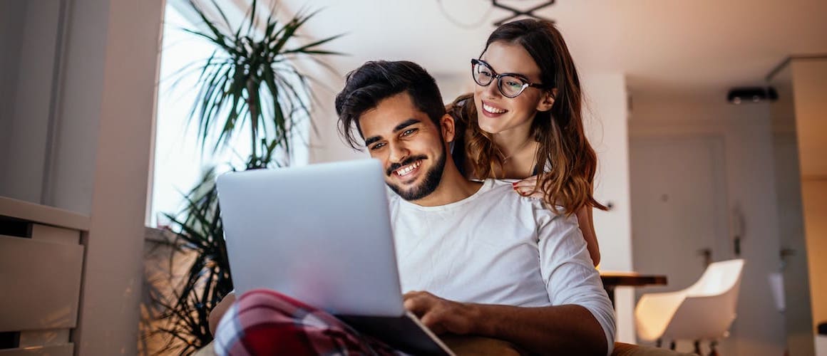 Young couple looking at homes online together, smiling.