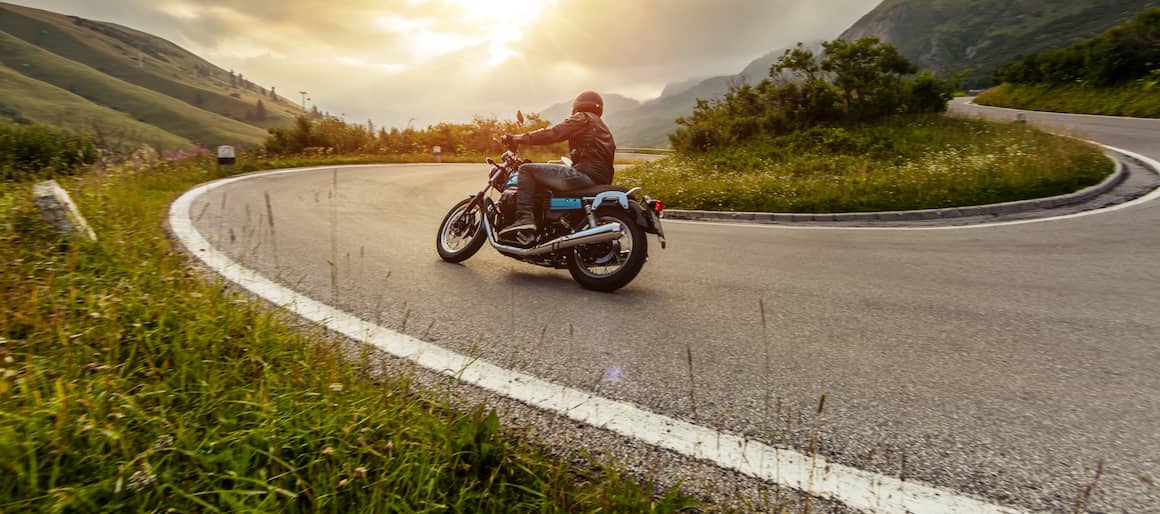 A person driving a motorcycle around a curve at sunset