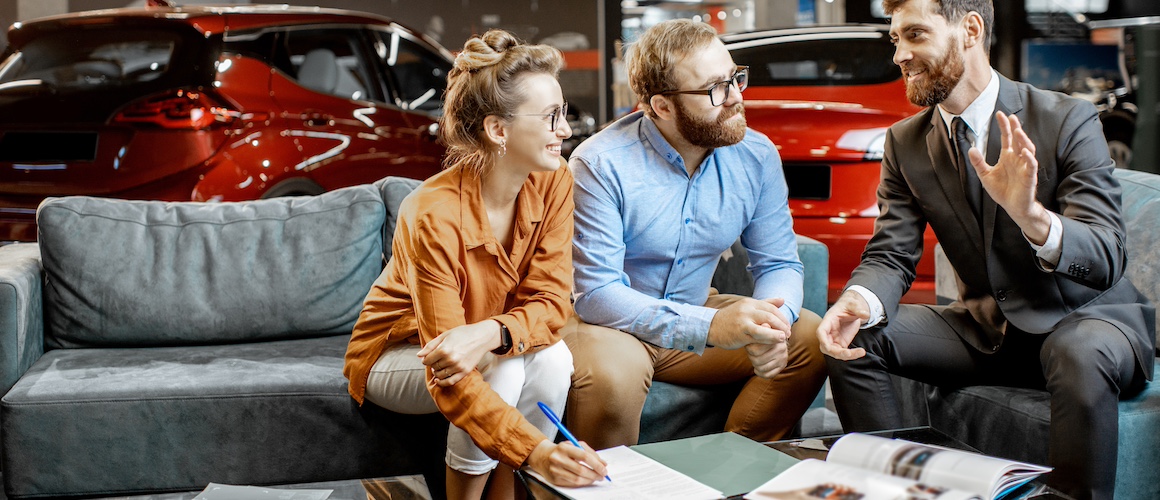 Young couple with sales manager on the comfortable couch at the car dealership. 