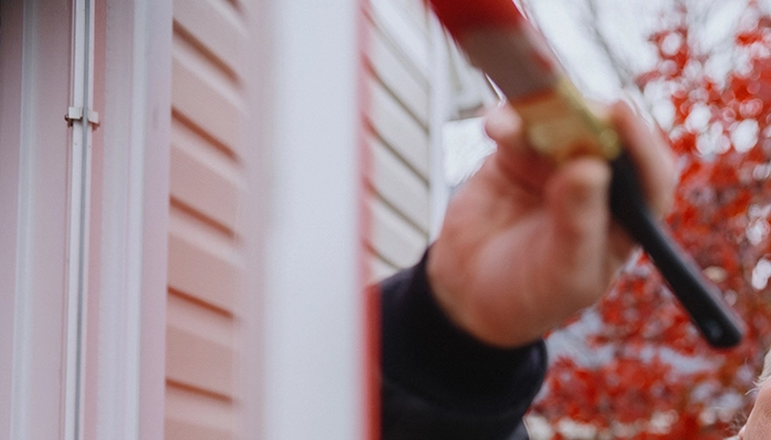 Man smiling painting door red with red tree in the background.