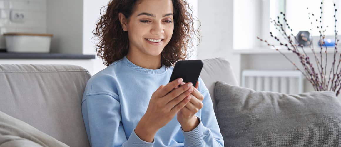 Image of woman on gray couch, smiling down at phone