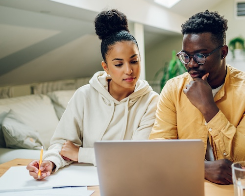 Couple reviewing bills on laptop and papers nearby.