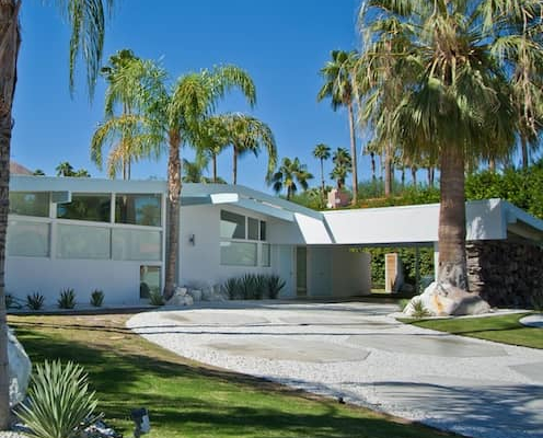 Palm Springs midcentury modern ranch style home in white with large front yard landscaped with palm trees.