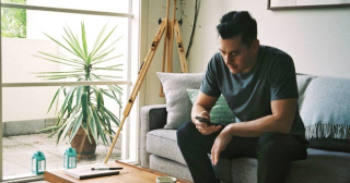 Man in his living room sitting on the couch looking at his mobile phone.