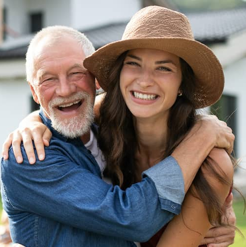 A woman hugging her father in front of a property possibly in woods.