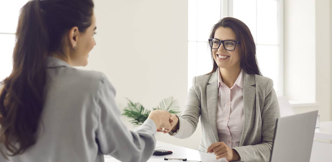 Two women shaking hands, indicating a successful agreement or partnership in real estate.