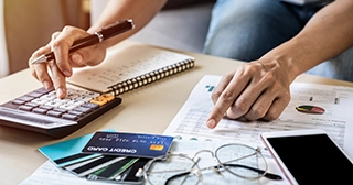 Image of a persons hands at desk with documents, credit cards and a calculator, tackling credit card bills.