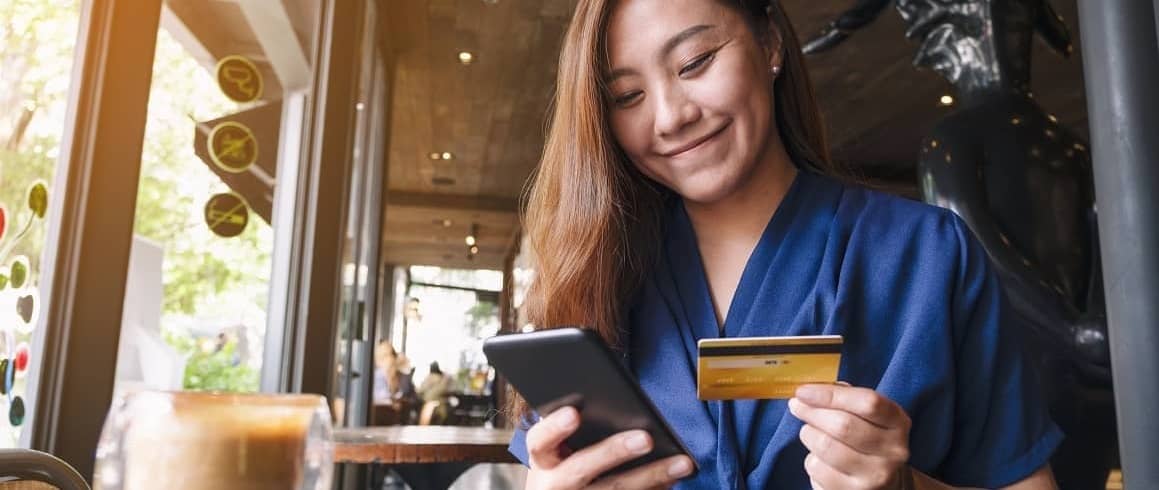 Woman smiling using credit card to pay bill on phone at cafe.