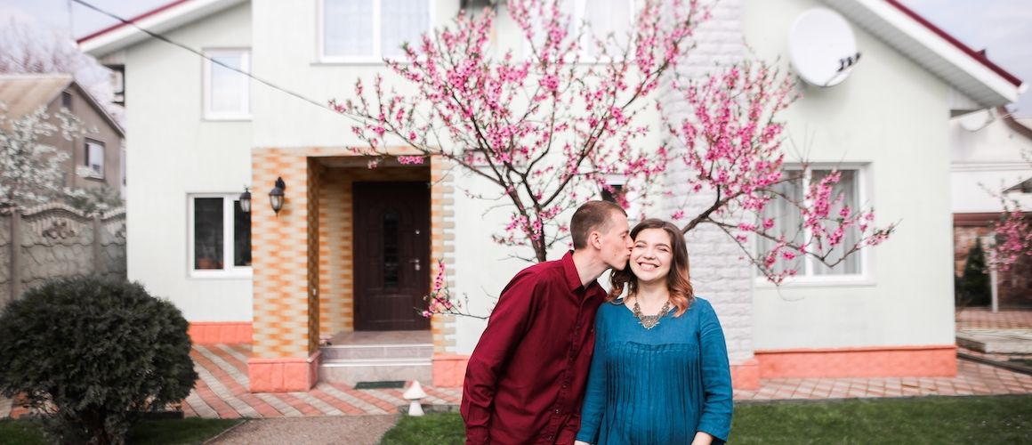 Couple standing in front of a house, portraying a couple standing proudly in front of a house, possibly theirs.
