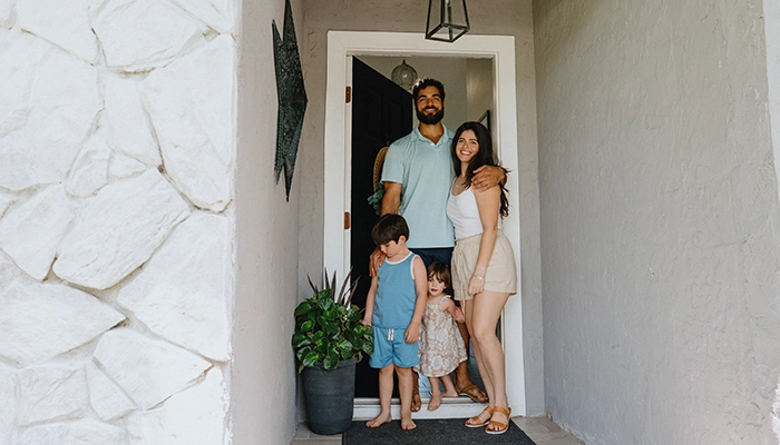 Family standing and smiling in front doorway.